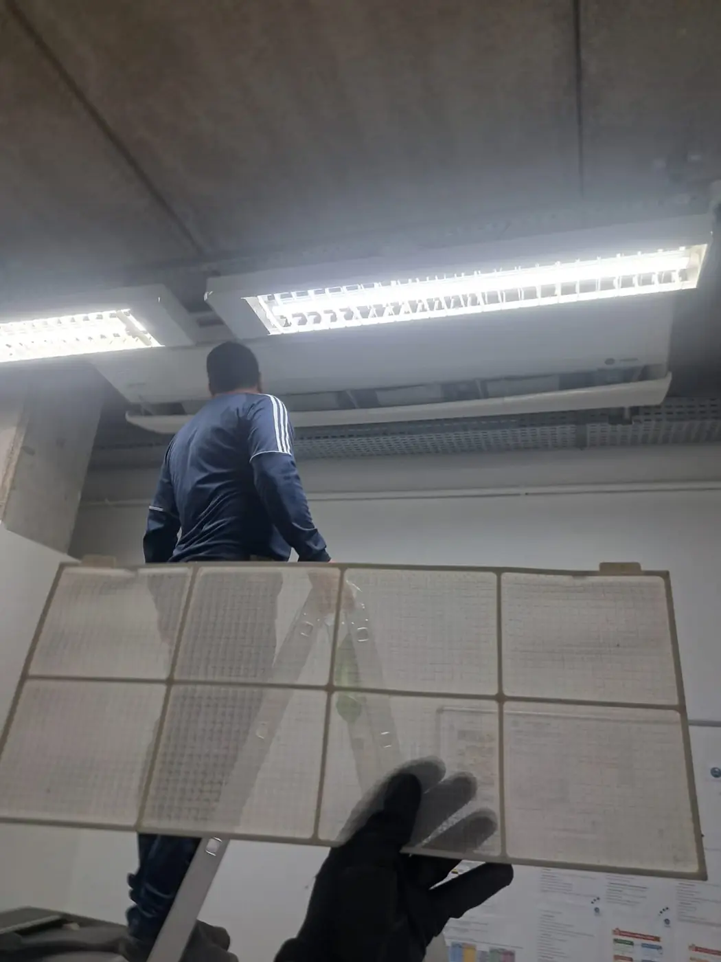 Técnico da Manprev segurando os filtros retirados de um aparelho de teto numa escola