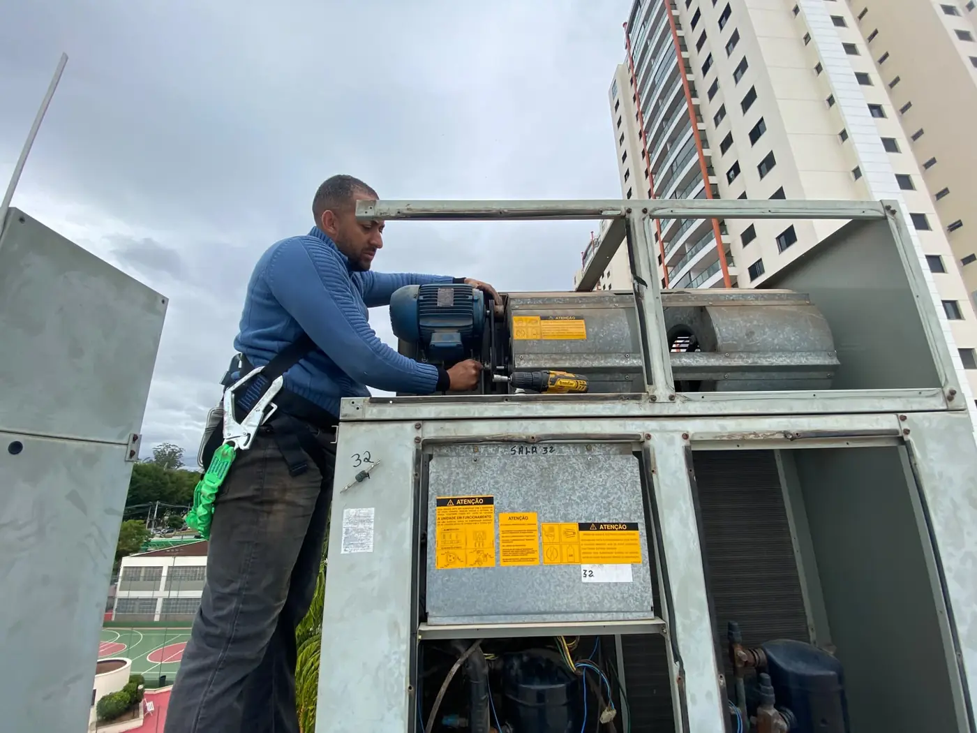 Técnico da Manprev, preso ao cinto de segurança, trabalhando no motor de um Splitão na cobertura de um prédio